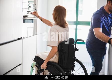 Vue latérale d'un mari méconnaissable dans des vêtements décontractés avec une femme handicapée en fauteuil roulant utilisant l'équipement moderne de l'hôpital Banque D'Images