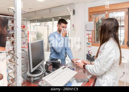 Pharmacien femelle méconnaissable en blouse de laboratoire blanche à l'écoute d'un homme malade avec le nez courant aidant au choix du médicament Banque D'Images
