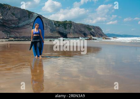 Corps complet de jeune athlète féminine regardant loin tout en s'appuyant sur la planche de surf contre l'eau de mer pendant l'été à la plage de Zarautz Banque D'Images