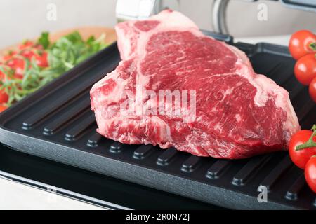 Steaks de première qualité crus sur le gril électrique. Steaks de viande de choix black angus Ribeye sur un grill électrique moderne au romarin, à la tomate cerise et au poivre. Cuisine pro Banque D'Images