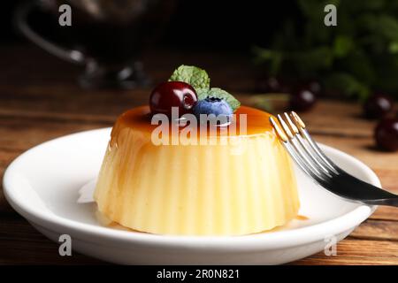 Assiette de délicieux pudding au caramel aux myrtilles, aux cerises et à la menthe servie sur une table en bois, en gros plan Banque D'Images