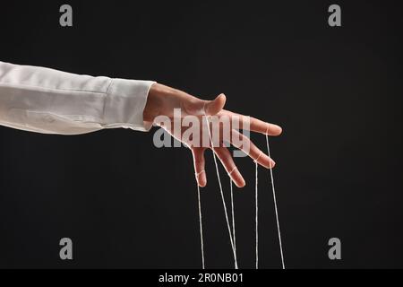 Femme tirant des cordes de marionnette sur fond noir, gros plan Banque D'Images