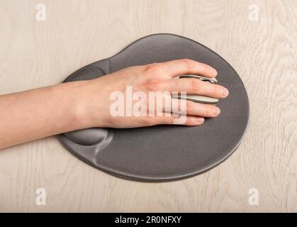 Main sur la souris d'ordinateur sur un bloc de gel ergonomique avec repose-poignet, repose sur un bureau. Banque D'Images