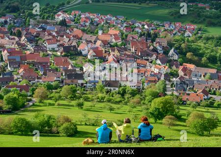 Trois personnes s'assoient dans la prairie et regardent le village de Kohlberg, Jusiberg, Jura souabe, Bade-Wurtemberg, Allemagne Banque D'Images