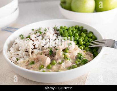 Fricassée de poulet au riz basmati et au riz sauvage. Servi avec des pois verts beurrés sur une assiette Banque D'Images