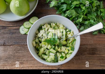 Salade de légumes aux fruits avec pommes vertes marinées et concombre dans un bol sur une table en bois Banque D'Images