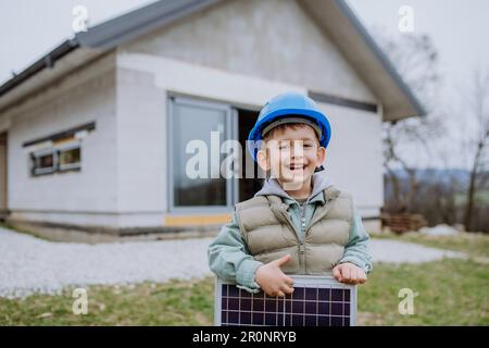 Portrait d'un petit garçon tenant un panneau solaire, devant leur nouvelle maison inachevée. Banque D'Images