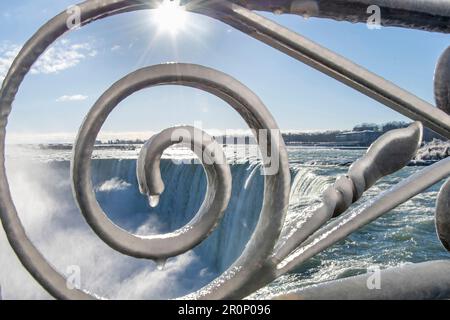 Gros plan de la clôture ornementale recouverte d'une épaisse couche de glace sur les chutes Niagara, ONTARIO, Canada, en hiver, avec des projections d'eau et des rayons lumineux du soleil Banque D'Images