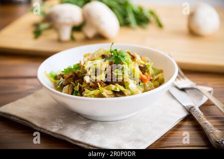 chou frit avec des champignons, des carottes et des légumes dans un bol blanc sur une table en bois Banque D'Images