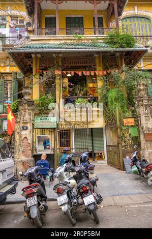 La façade d'une vieille maison de ville avec des vélomoteurs garés en face dans la vieille partie de Hanoi, Vietnam. Banque D'Images