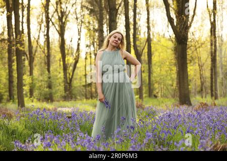 Une femme debout dans un bois de bluebell portant une longue robe verte Banque D'Images