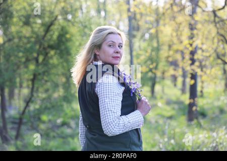 Une femme debout dans un bois de bluebell tenant un groupe de bluebells Banque D'Images