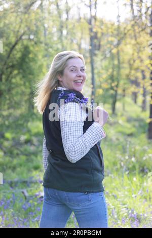 Une femme debout dans un bois de bluebell tenant un groupe de bluebells Banque D'Images