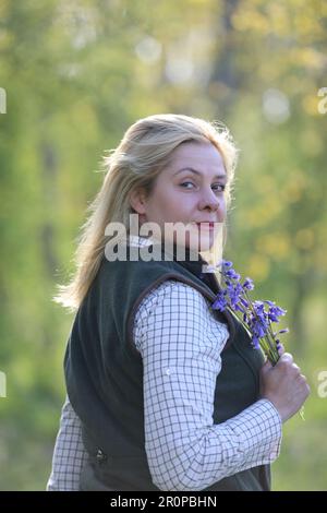 Une femme debout dans un bois de bluebell tenant un groupe de bluebells Banque D'Images