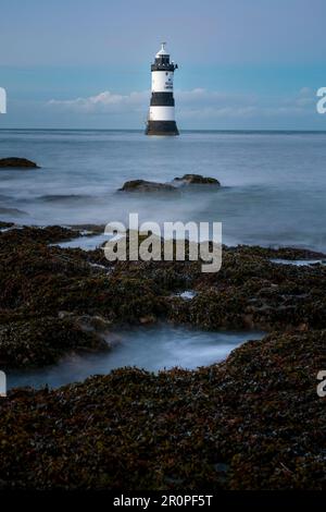 Un phare pittoresque de Penmon point, à Anglesey, debout sur un rivage rocheux contre un ciel nuageux Banque D'Images