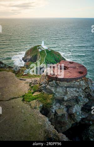 Une vue panoramique sur une falaise avec une herbe verte luxuriante et un petit phare blanc de South Stack Banque D'Images
