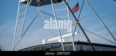 Deux échelles et cadre en aluminium de la tour Tpas au-dessus d'un yacht de pêche sportive et d'un drapeau américain, avec un fond de ciel principalement bleu. Banque D'Images