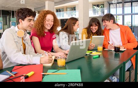 Des camarades de classe souriants utilisant des ordinateurs portables dans la cafétéria du campus. Groupe d'étudiants joyeux. Banque D'Images