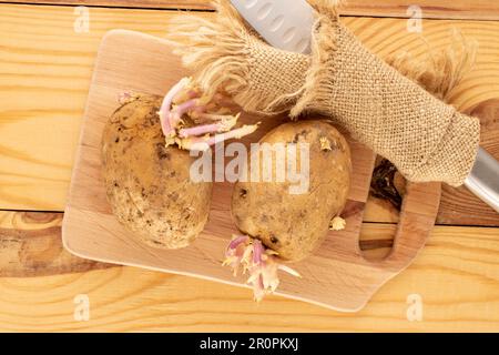 Deux pommes de terre avec des pousses avec un couteau en métal sur une cuisine en bois sur une table en bois, macro, vue de dessus. Banque D'Images