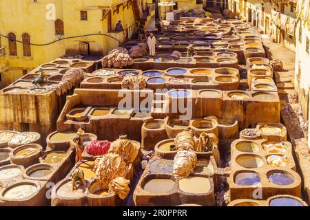 FES, Maroc - 31 mars 2023: Vue de la tannerie de cuir avec des cuves en pierre remplies de couleurs diverses, et des ouvriers. FES, Maroc Banque D'Images