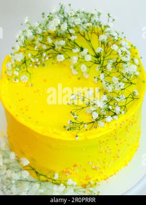 photo de studio de gâteau de célébration jaune givré avec fleurs blanches sauvages isolées sur fond blanc Banque D'Images