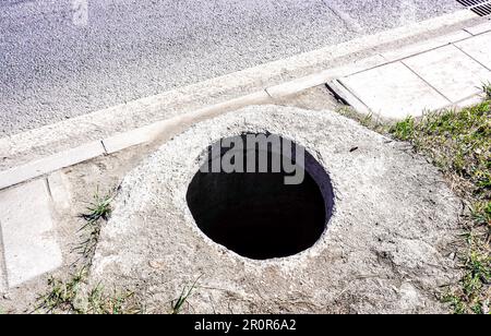 Ouvrir un trou d'homme non sécurisé sur le côté d'une route en asphalte. Fosse dangereuse sur la route. Trappe de puits d'égout sur la rue Banque D'Images