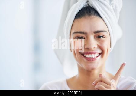 La peau éclatante commence par les bonnes habitudes de soin de la peau. Portrait d'une belle jeune femme appliquant un hydratant sur sa peau dans la salle de bains à la maison. Banque D'Images