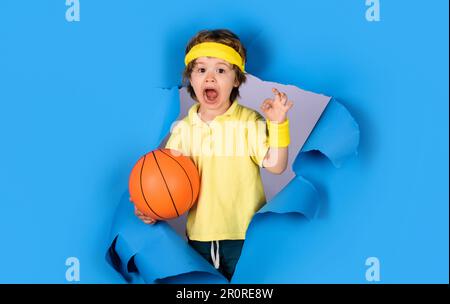 En jouant au sport. Petit ballon de basket-ball avec affiche ok. Enfant garçon dans les vêtements de sport avec ballon de basket-ball montre un geste correct Banque D'Images