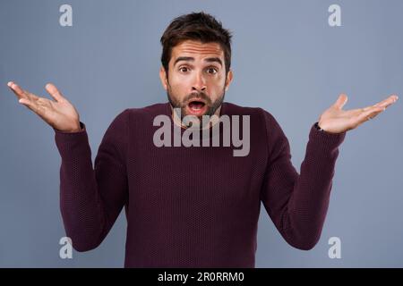 Qu'est-ce que cela signifie même ? Photo studio d'un beau jeune homme à l'air surpris sur fond gris. Banque D'Images