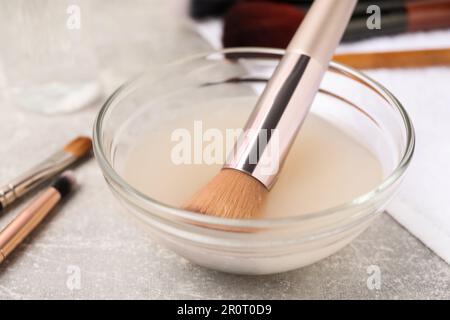 Brosse à maquillage dans un bol avec nettoyant sur table grise, gros plan Banque D'Images