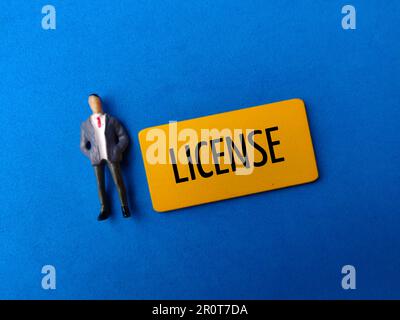 Personnes miniatures et panneau en bois coloré avec le mot LICENCE sur fond rouge Banque D'Images