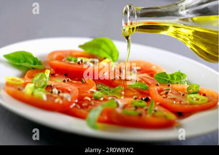 Verser l'huile d'olive sur une salade de tomates et de basilic Banque D'Images