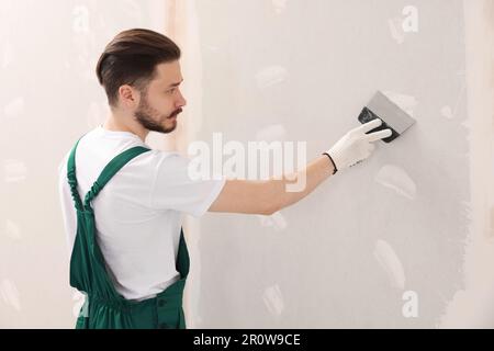 Travailleur dans un mur uniforme de plâtrage avec couteau à mastiquer à l'intérieur Banque D'Images