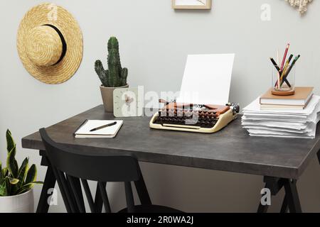 Machine à écrire et pile de papier sur table sombre dans la chambre. Lieu de travail du rédacteur Banque D'Images