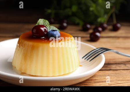 Assiette de délicieux pudding au caramel aux myrtilles, aux cerises et à la menthe servie sur une table en bois, en gros plan Banque D'Images