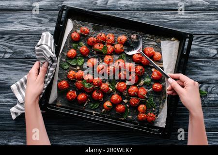 Woman pouring sauce sur les tomates cuites dans le moule sur une table en bois foncé Banque D'Images