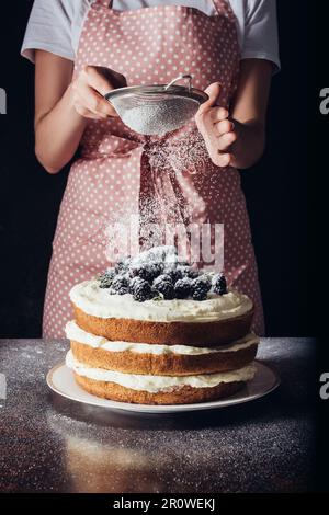 Femme qui a versé de la poudre de sucre sur un BlackBerry savoureux sur du noir Banque D'Images