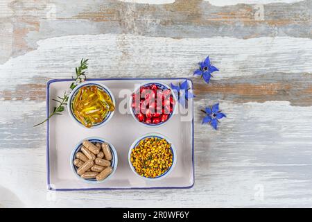 Capsules de complément alimentaire, pollen d'abeille et graines de grenade dans des bols Banque D'Images