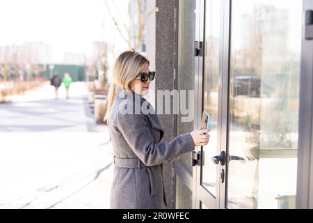 Une femme utilise le balayage du téléphone pour se rendre aux systèmes de sécurité à verrouillage numérique des portes à la maison. Banque D'Images