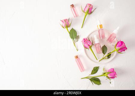 Huile de rose et eau dans diverses bouteilles de verre sur un plateau de plâtre blanc parmi les roses vivantes. cosmétiques naturels biologiques pour les soins personnels. Un espace de copie Banque D'Images