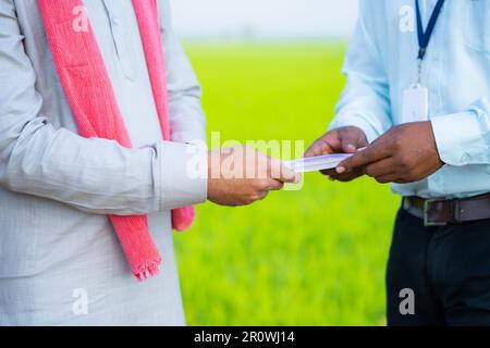 Gros plan sur le paysan du village recevant de l'argent du banquier sur les terres agricoles vertes - concept de prêt de l'agro-industrie, soutien financier et investissement Banque D'Images