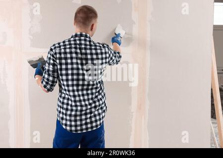 Homme plâtrage mur avec couteau à mastiquer à l'intérieur, vue arrière et espace pour le texte. Rénovation de la maison Banque D'Images