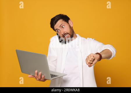 Homme émotionnel avec ordinateur portable parlant au téléphone sur fond orange. Être un concept tardif Banque D'Images