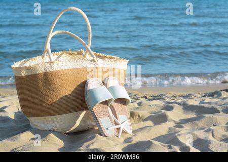 Sac de paille, pantoufles et étoiles de mer sèches sur une plage de sable près de la mer, espace pour le texte Banque D'Images