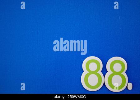 Le numéro 88 de couleur bleu foncé et vert, photographié par le dessus, est placé sur le bord d'un fond bleu. Banque D'Images