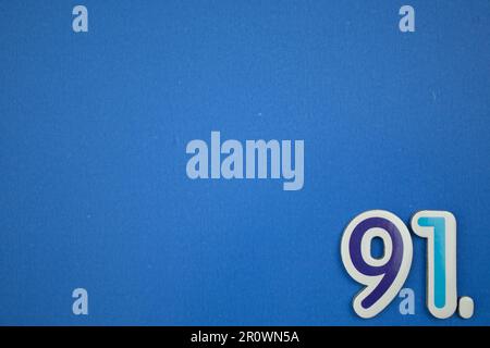 Le numéro 91 de couleur bleu clair, photographié par le dessus, est placé sur le bord d'un fond bleu. Banque D'Images