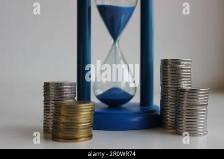 Le temps, c'est de l'argent. Les pièces de monnaie dans les colonnes entourent un sablier avec le sable tombant Banque D'Images