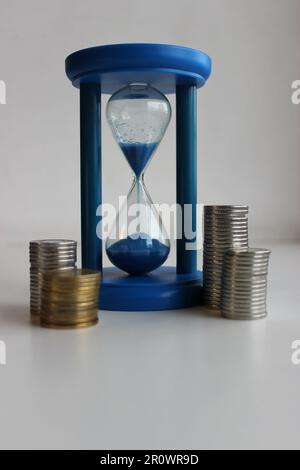 Verre de sable bleu et pièces de monnaie alignés en colonnes sur un fond blanc photo verticale Banque D'Images