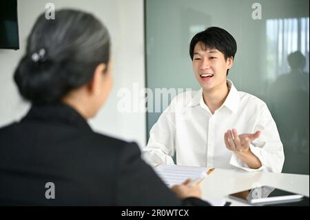 Jeune homme asiatique confiant et intelligent répondant à des questions et parlant de ses expériences de carrière à un recruteur d'emploi lors d'une entrevue d'emploi. Banque D'Images