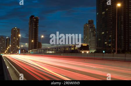 train électrique avec des sentiers légers sur l'autoroute au crépuscule. Entraînez-vous avec la ville en toile de fond. Banque D'Images